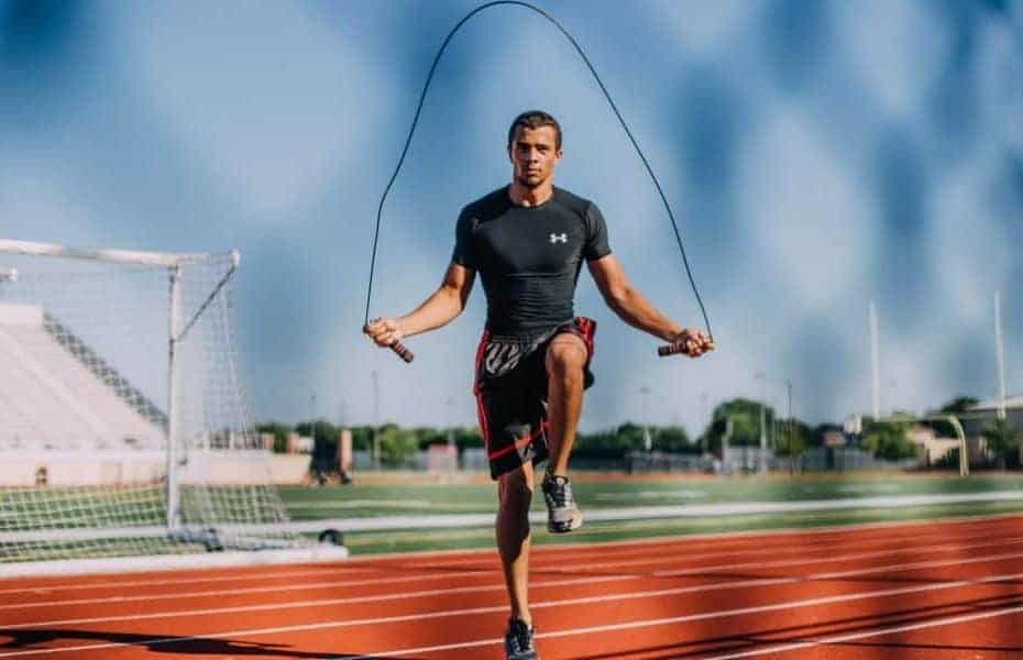 Un uomo che esegue esercizi di gioco di gambe con una corda per saltare su una pista.